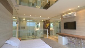 A modern hotel room with a bed, a desk, a TV, and a glass-enclosed bathroom. - Le Ville (Ouro Preto)