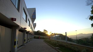 A modern building with numbered doors, a paved walkway, and a view of distant hills during sunset. - Le Ville (Ouro Preto)