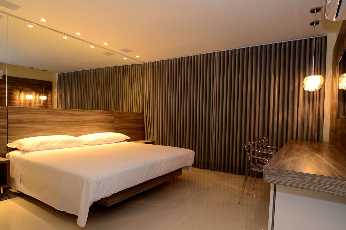 A modern bedroom with a wooden headboard, a large bed with white bedding, a bedside table, and a built-in TV.