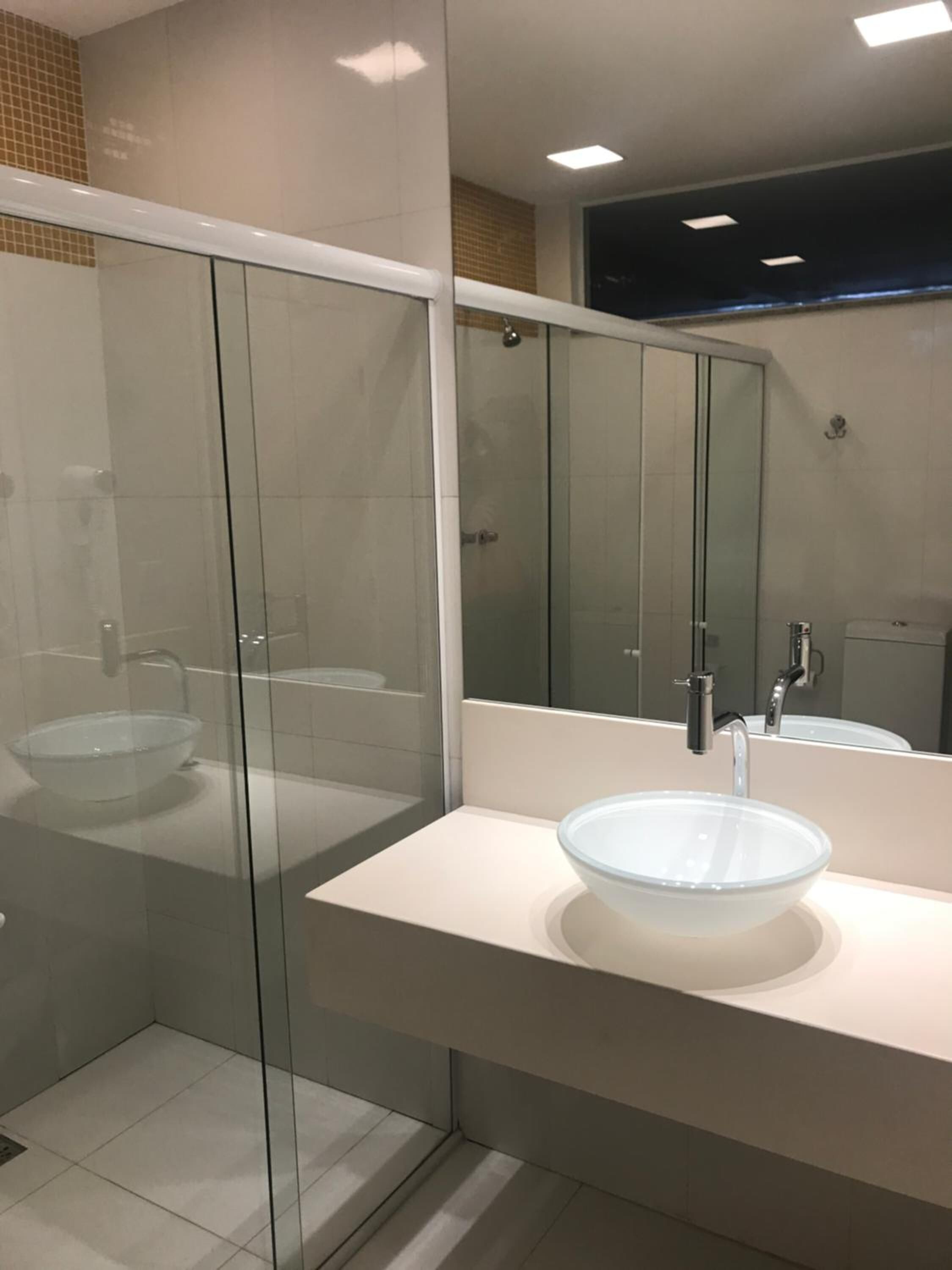 A modern bathroom with a glass-enclosed shower, a white sink with a glass bowl, and a large mirror.