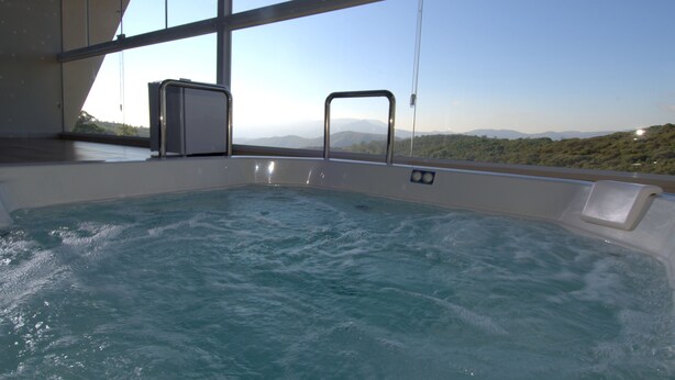 A hot tub with a clear view of mountains through large windows. - Le Ville (Ouro Preto)