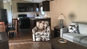 A living room with a sofa, a floral armchair, a coffee table, and a kitchen area with dark cabinets and a microwave. - QuickStay - Heavenly Cottage (Beautiful Lake Views) (Bracebridge)
