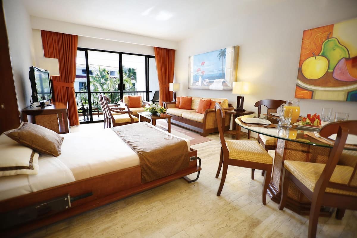 Una habitació d'hotel amb un llit, un sofà, una taula de dinar amb cadires, un televisor i un quadre a la paret.