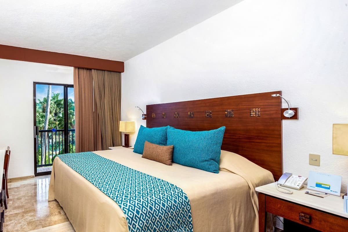 Habitació d'hotel amb llit, escriptori amb ordinador, televisió i un balcó amb cortines.