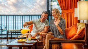 Una pareja sentada en una mesa con desayuno en un balcón con vistas al mar.