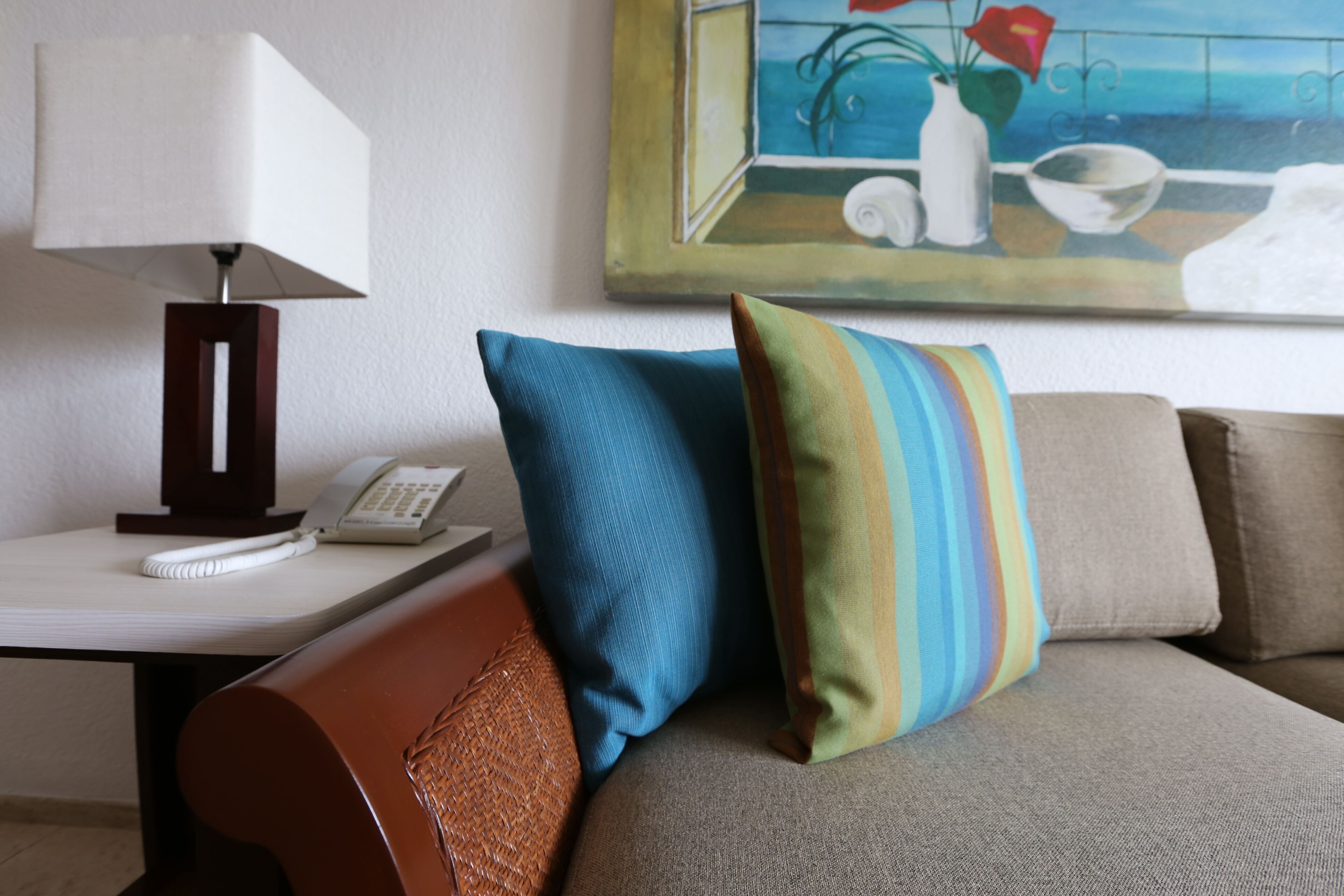 A hotel room with a sofa, a lamp, a painting, and a telephone on a side table.