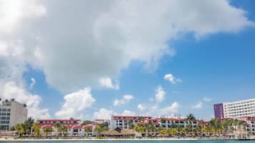 Un hotel frente a la playa con varias edificaciones de techos rojos, palmeras y un cielo azul despejado.