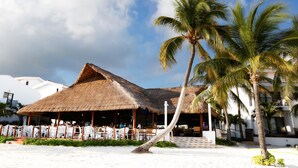 Un resort frente a la playa con estructuras de techo de paja, palmeras y una playa de arena.