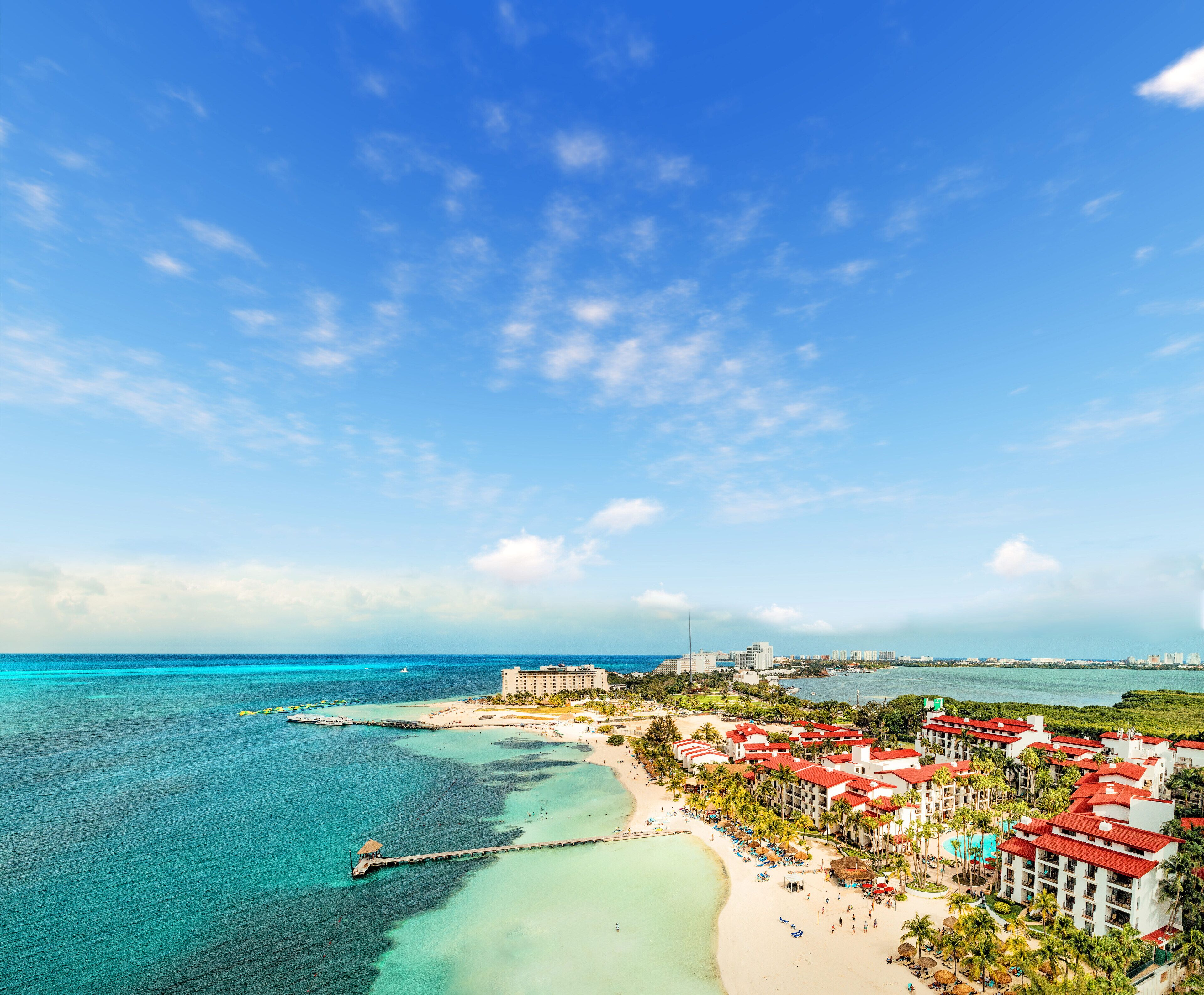 A coastal resort with a pier extending into turquoise waters, beachfront villas, and a clear view of the ocean.