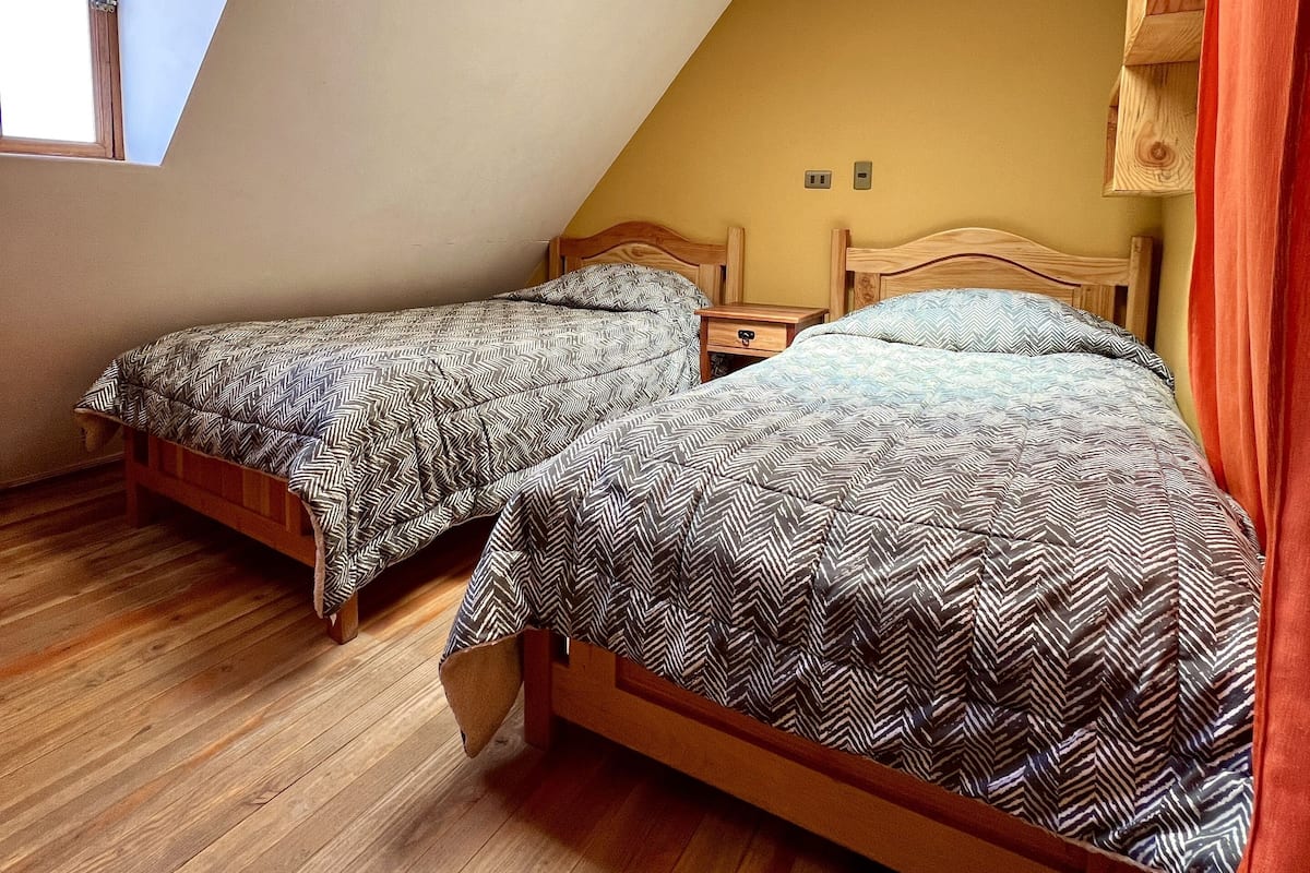 Une chambre avec deux lits en bois, une lucarne et un plancher en bois.