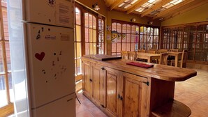 Une cuisine avec des meubles de rangement en bois, un réfrigérateur et un grand îlot central surmonté d’un set de table rouge.