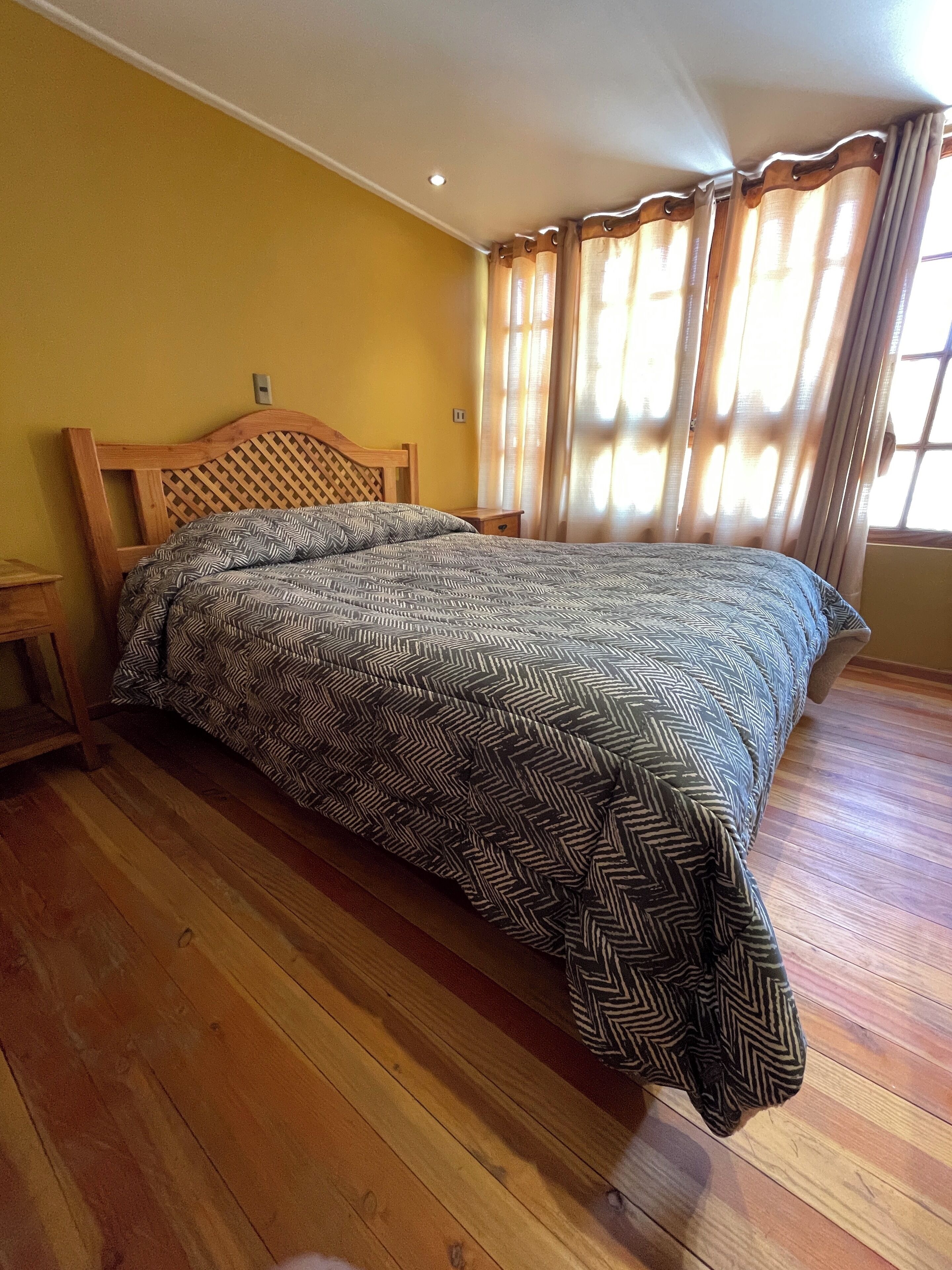 A bedroom with a wooden bed frame, a patterned bedspread, and wooden flooring.