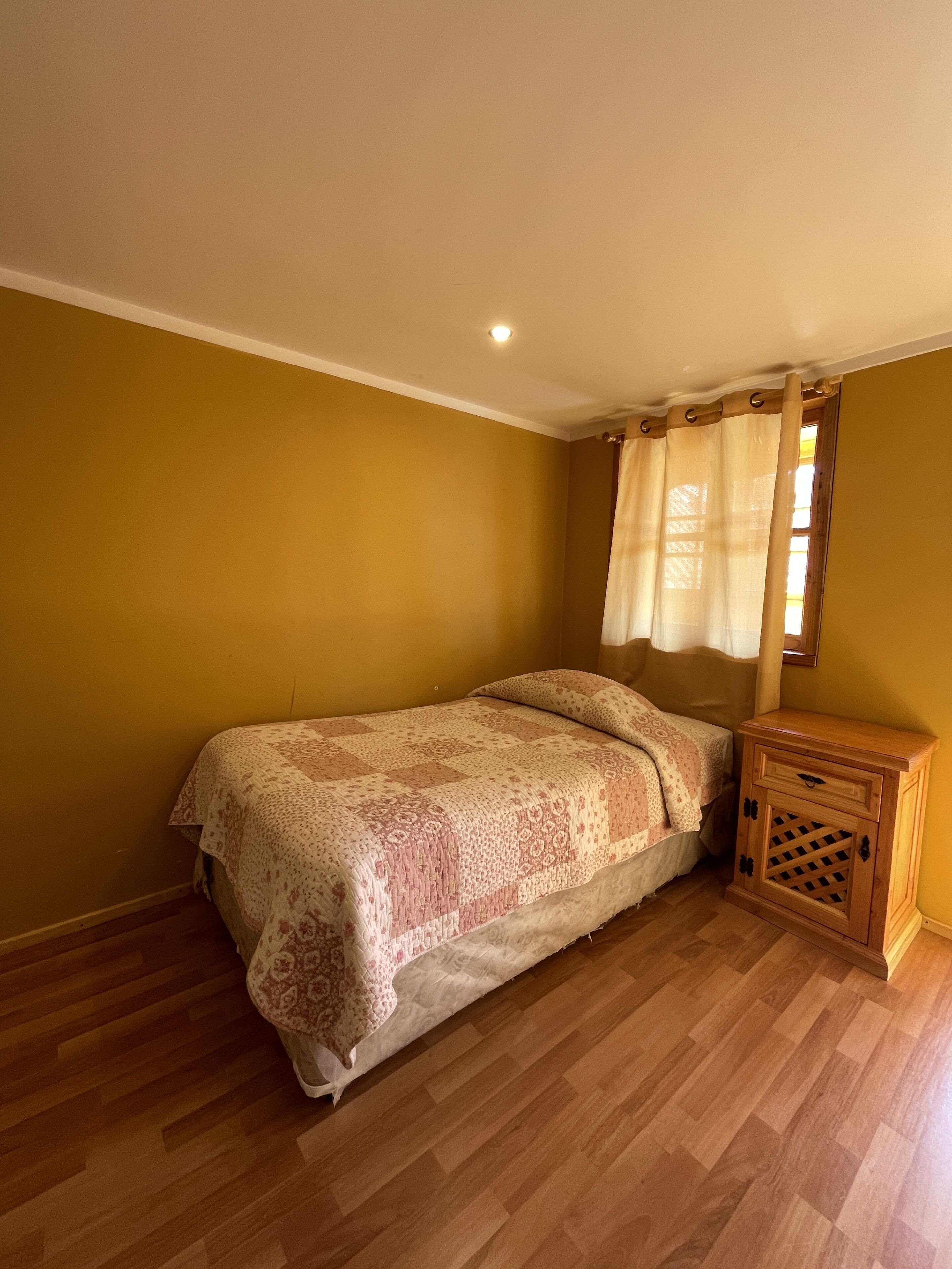 A bedroom with a bed, wooden nightstand, and a window with curtains.