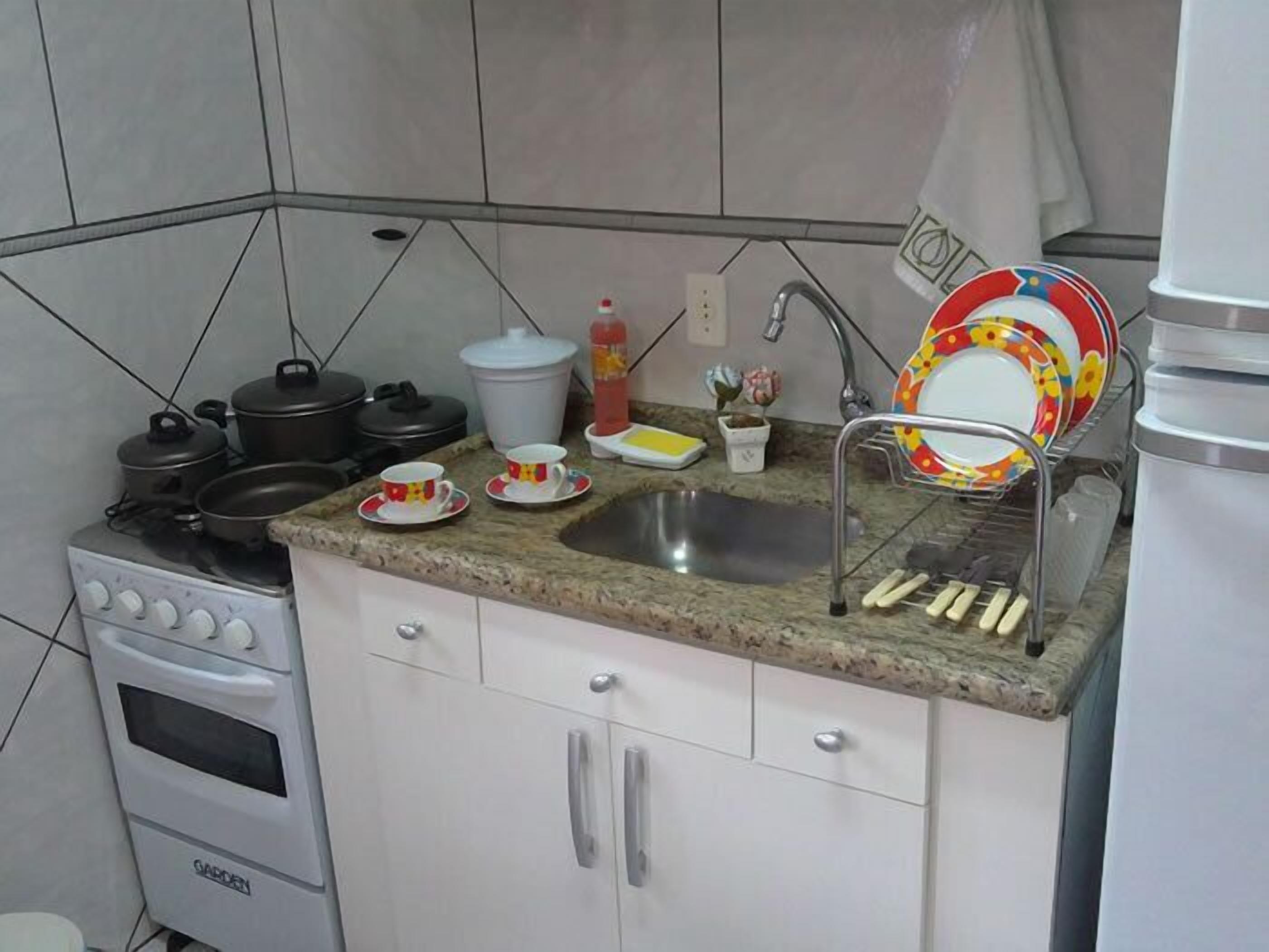 A kitchen with a stove, sink, and cabinets. There are pots, pans, and a kettle on the stove. A bottle of ketchup and a small plant are on the counter.