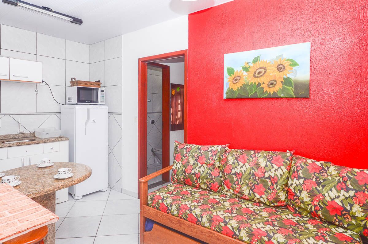 A compact living space with a kitchenette, a red wall with a sunflower painting, and a floral sofa.