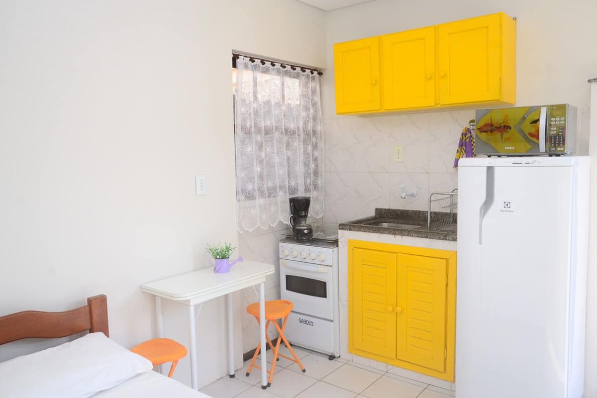 Une cuisine de taille réduite avec des placards jaunes, un réfrigérateur blanc, une cuisinière et une petite table avec une chaise.