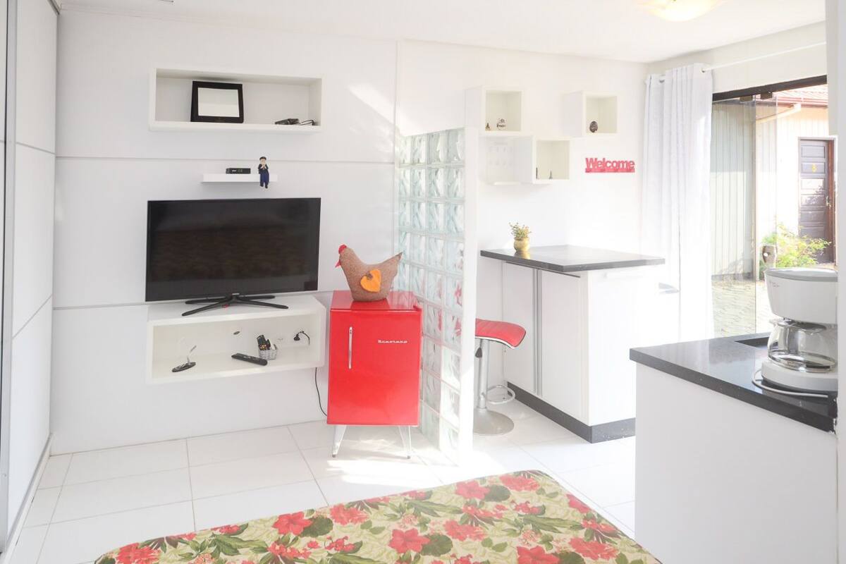 Une chambre d’hôtel moderne dotée d’une télévision à écran plat, d’un mini-bar rouge, d’un petit coin cuisine et d’un balcon avec vue.