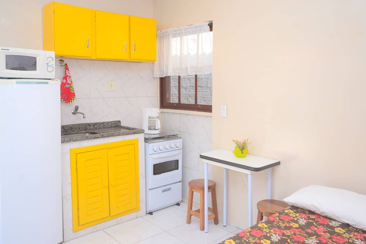 Une cuisine de taille réduite avec des meubles de couleur jaune, un micro-ondes blanc, une cuisinière et une petite table accompagnée d’un tabouret.