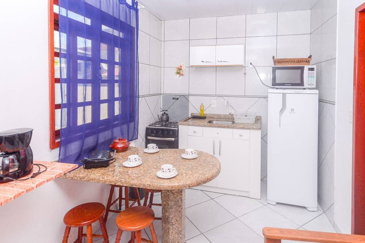 Une cuisine compacte avec des meubles blancs, un four à micro-ondes, une cuisinière à gaz et une petite table à manger avec des tabourets.