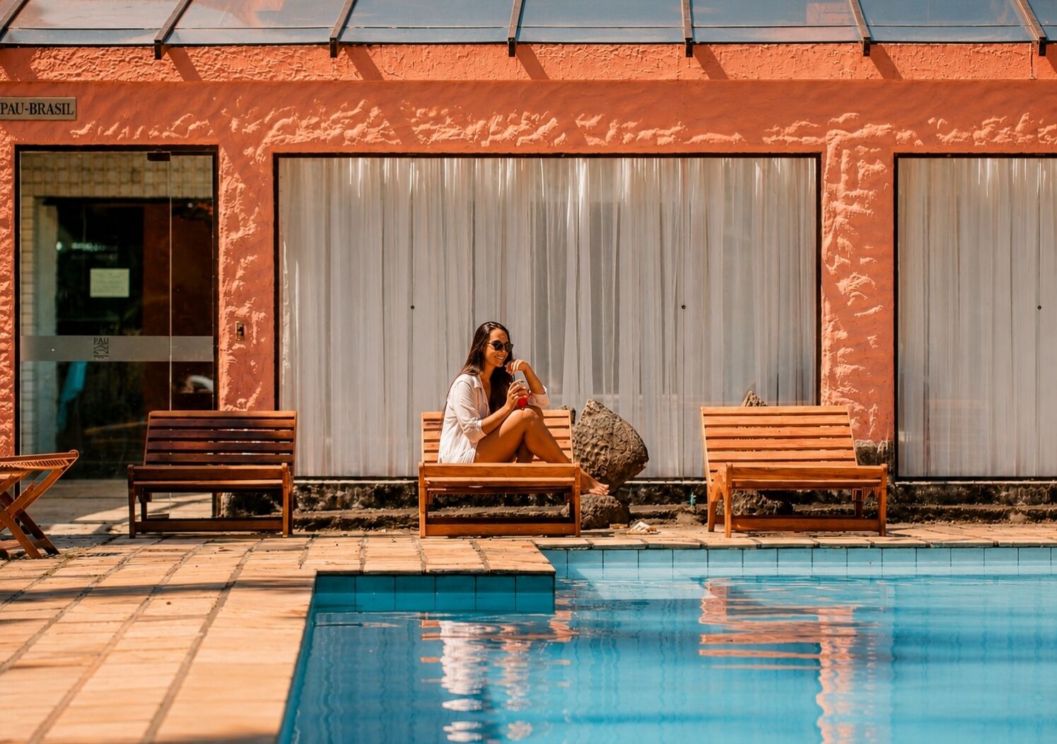 Zona de piscina con bancos de madera y una persona sentada en uno.