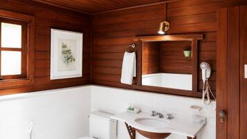 Un baño con paneles de madera, inodoro blanco, lavabo con encimera de mármol, espejo y secador de pelo en la pared.