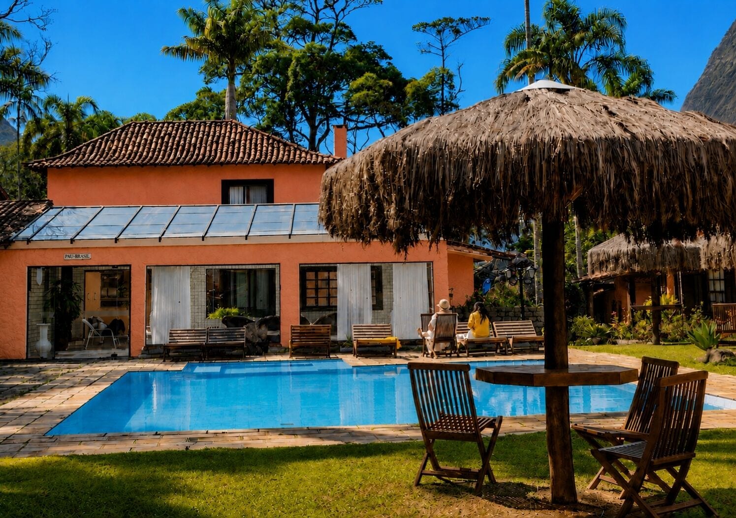 Una casa con piscina, mobiliario exterior y un toldo de paja.