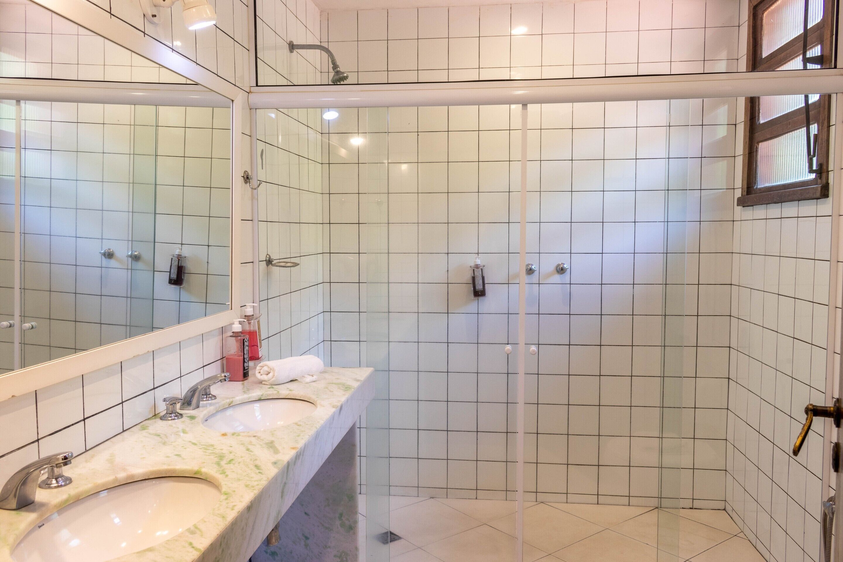 A bathroom with a glass-enclosed shower, a sink with a marble countertop, and a large mirror.