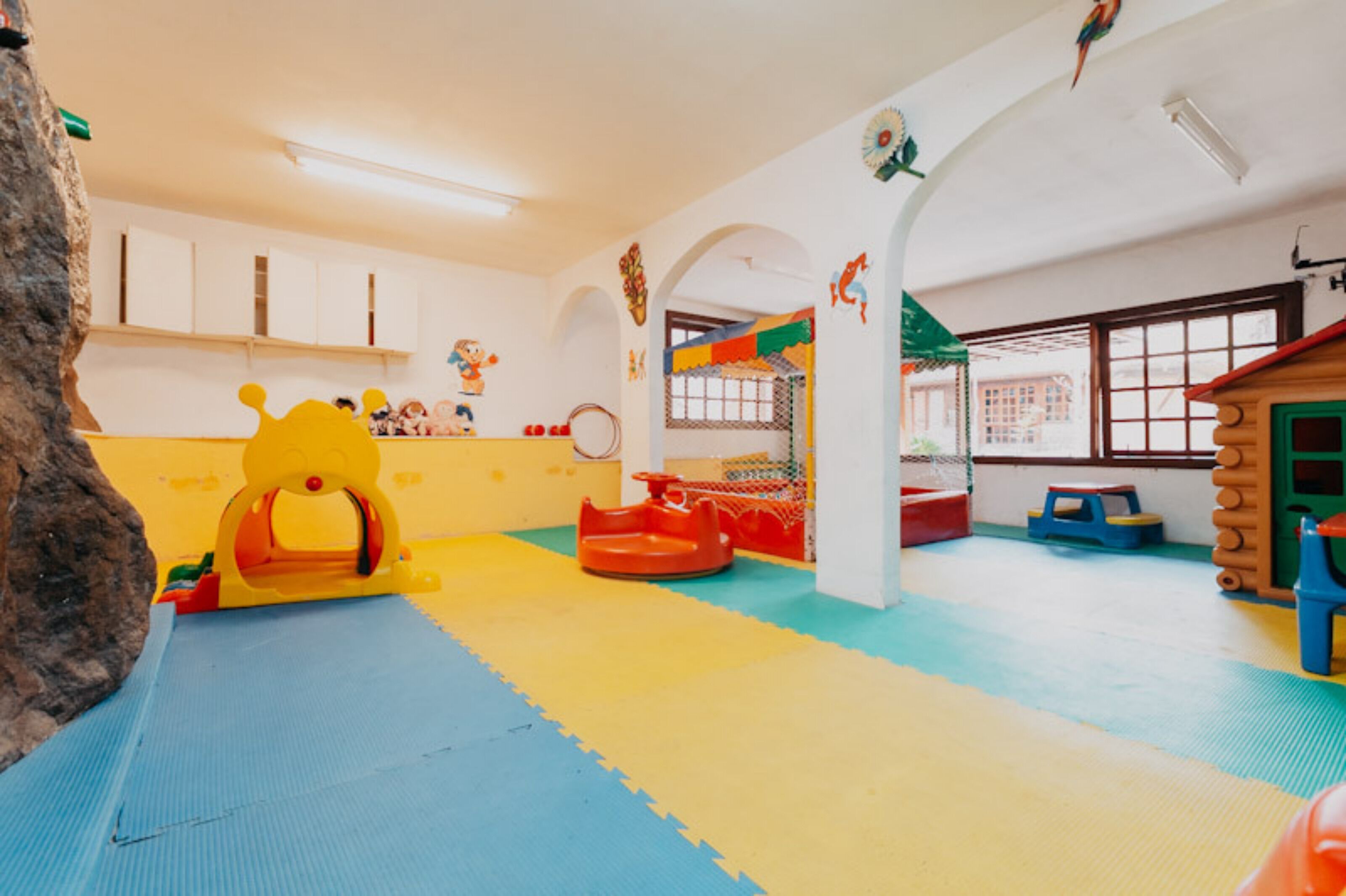A playroom with colorful mats, a yellow play structure, and a log cabin playhouse.
