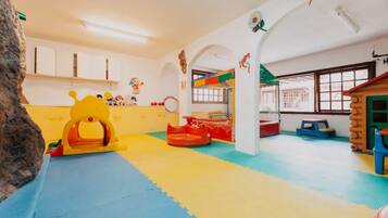 A playroom with colorful mats, a yellow play structure, and a log cabin playhouse.