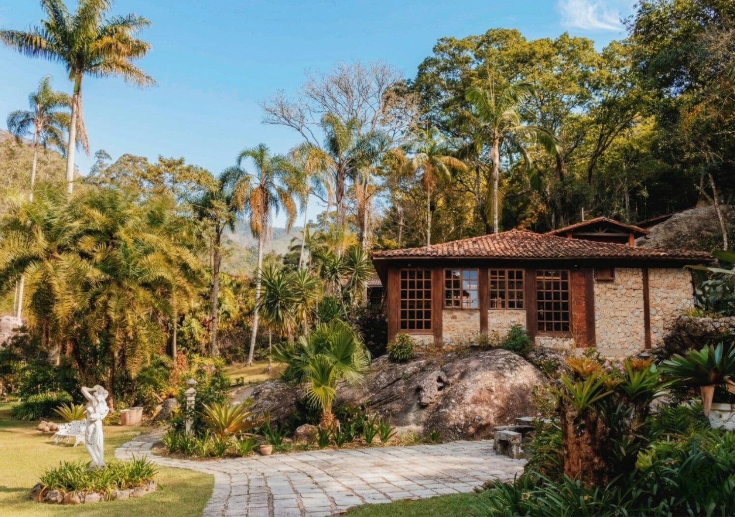 Un edificio de piedra con techo de tejas, rodeado de abundante vegetación y palmeras.