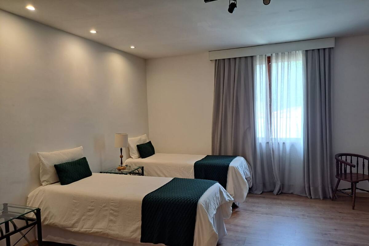 A hotel room with two beds, a chair, a table, and a window with curtains.