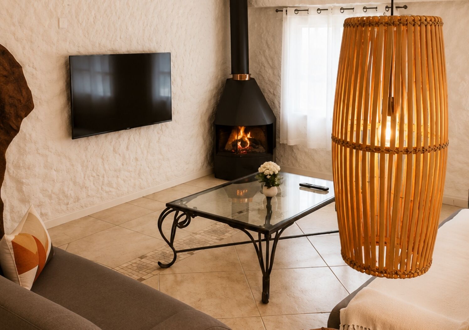 A living room with a flat-screen TV, a fireplace, a glass coffee table, a sofa, and a hanging wicker chair.