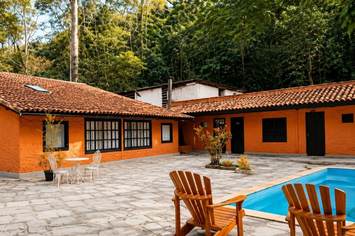 A courtyard with a swimming pool, wooden chairs, and a table.