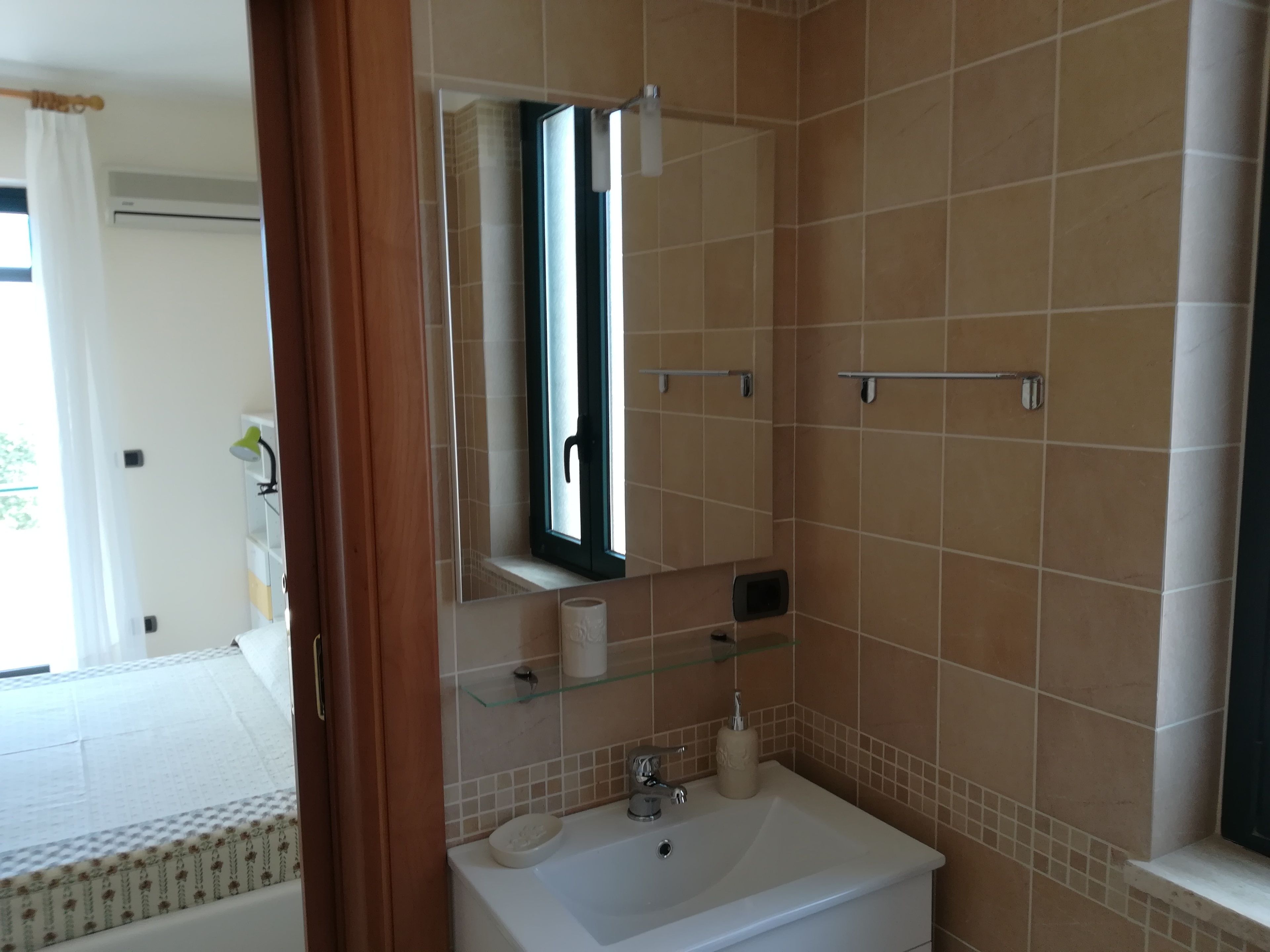 A bathroom with a white sink, a mirror, a glass shelf, and a window.