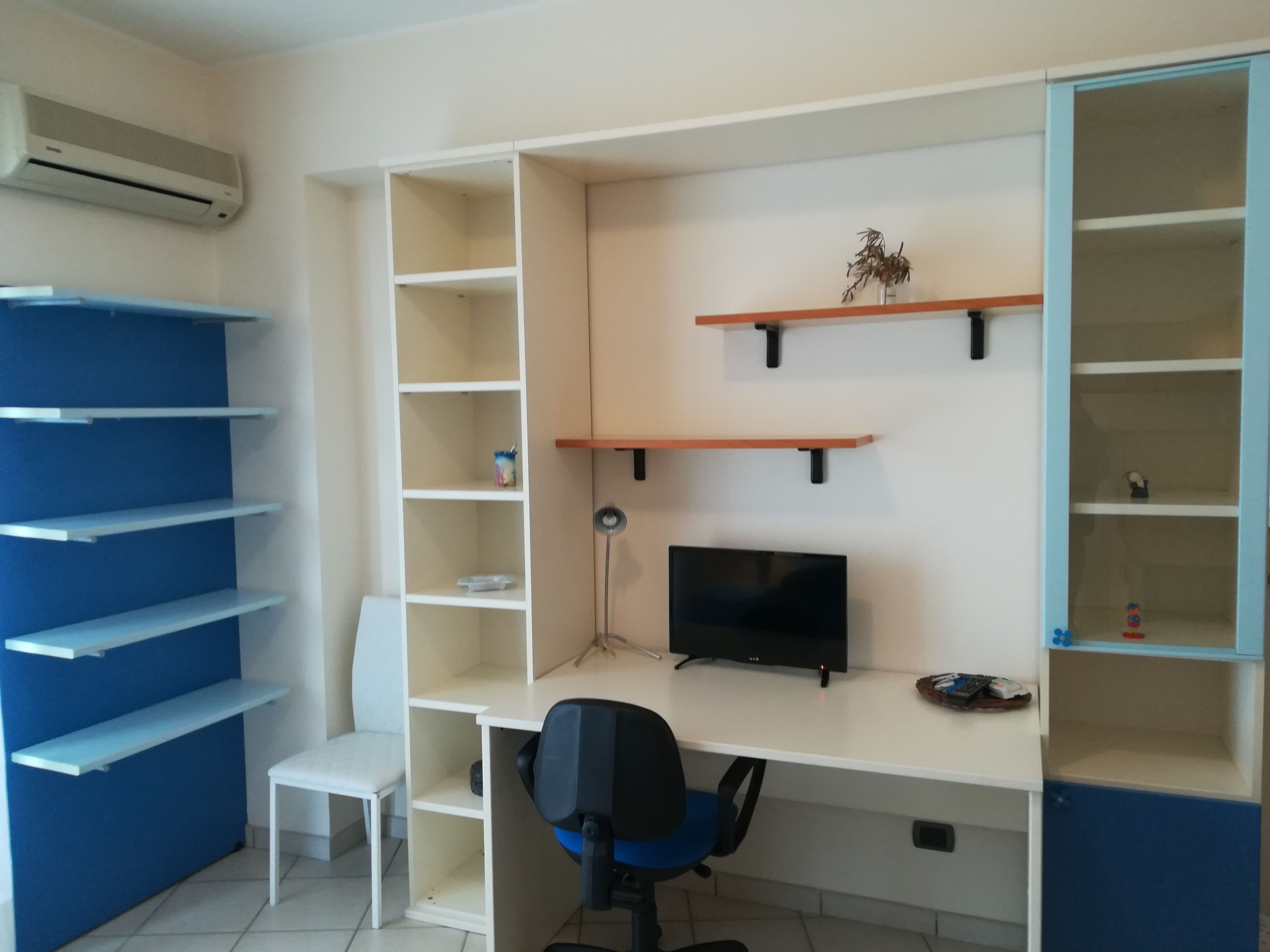 Un espacio de oficina moderno con escritorio, silla, estanterías y un equipo de aire acondicionado.