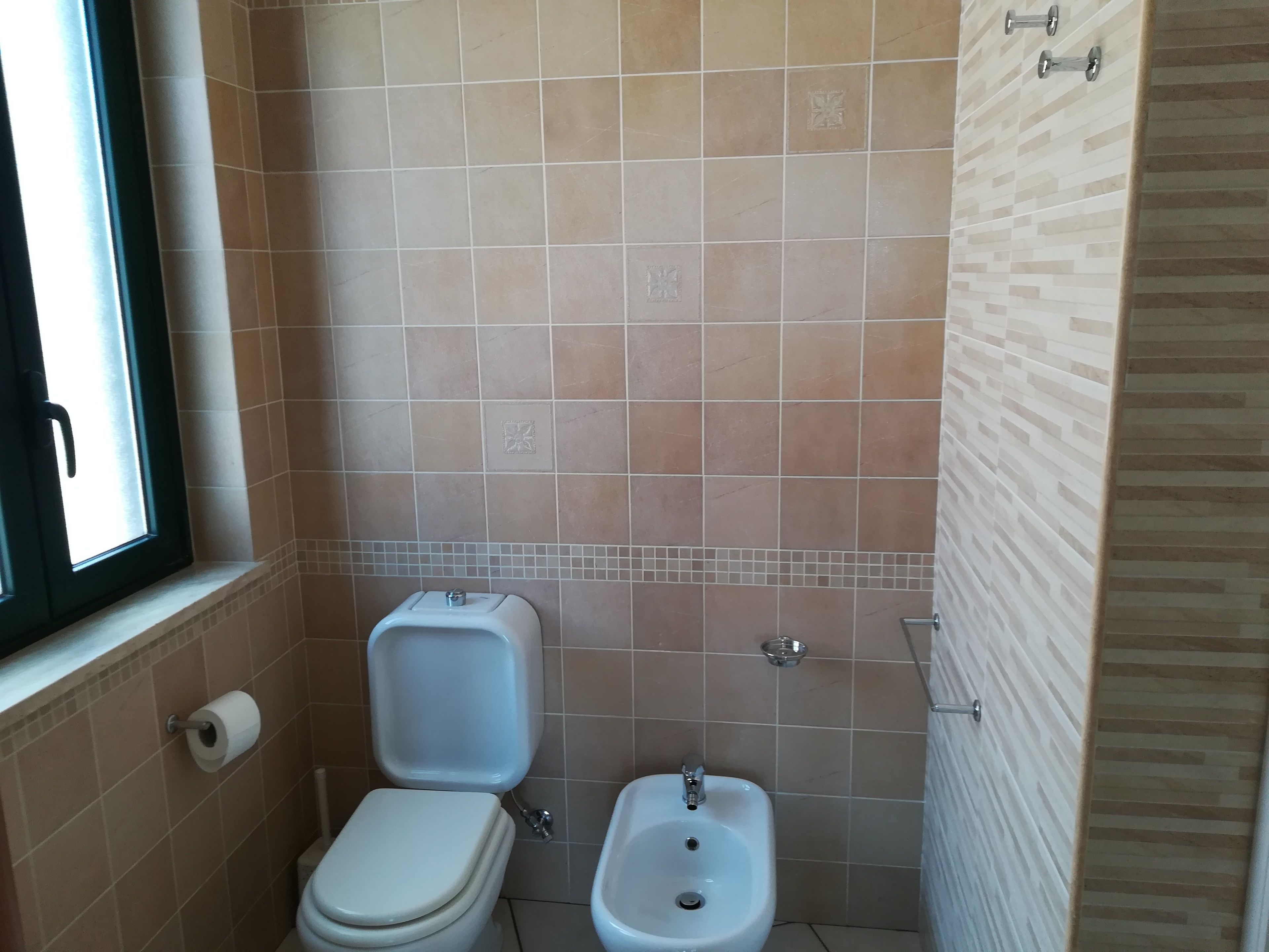 A small bathroom with a toilet, bidet, and a window.