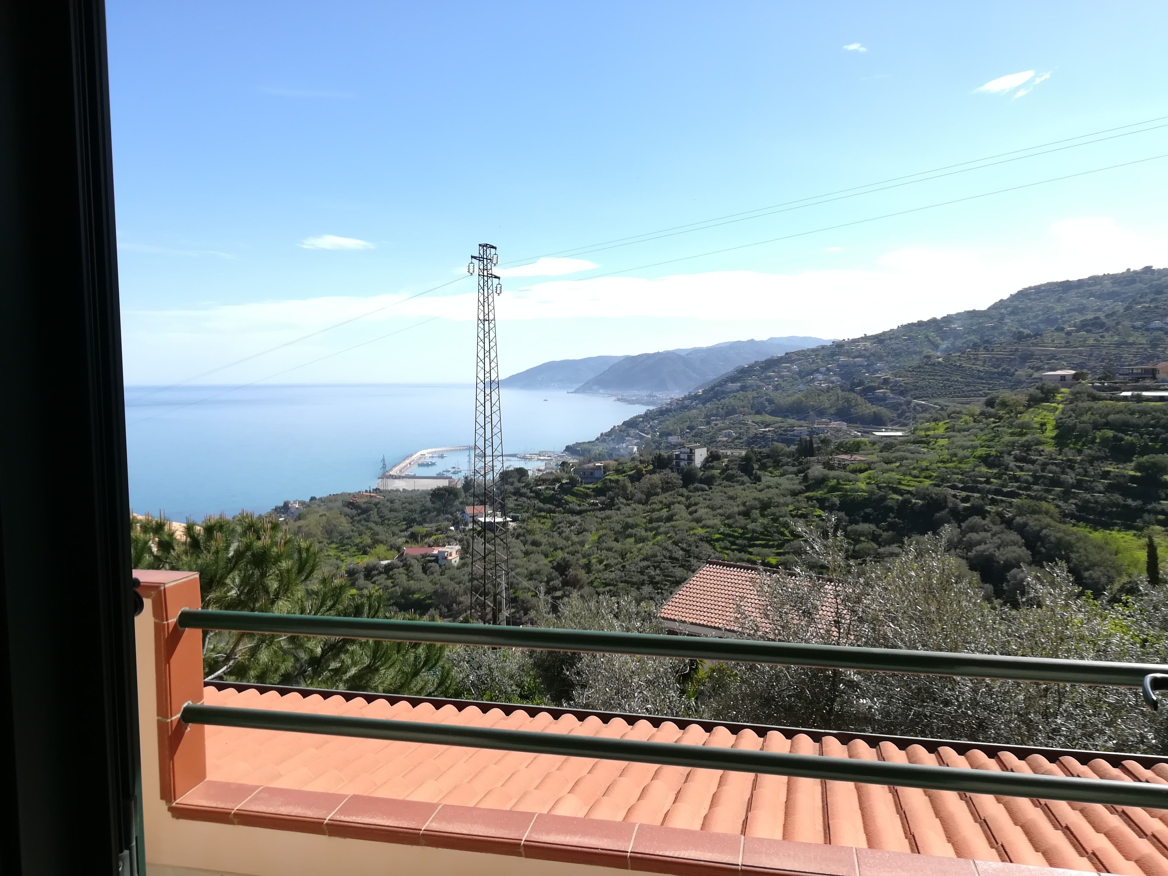A balcony with a view of a coastal landscape, including a power line tower and a distant shoreline.