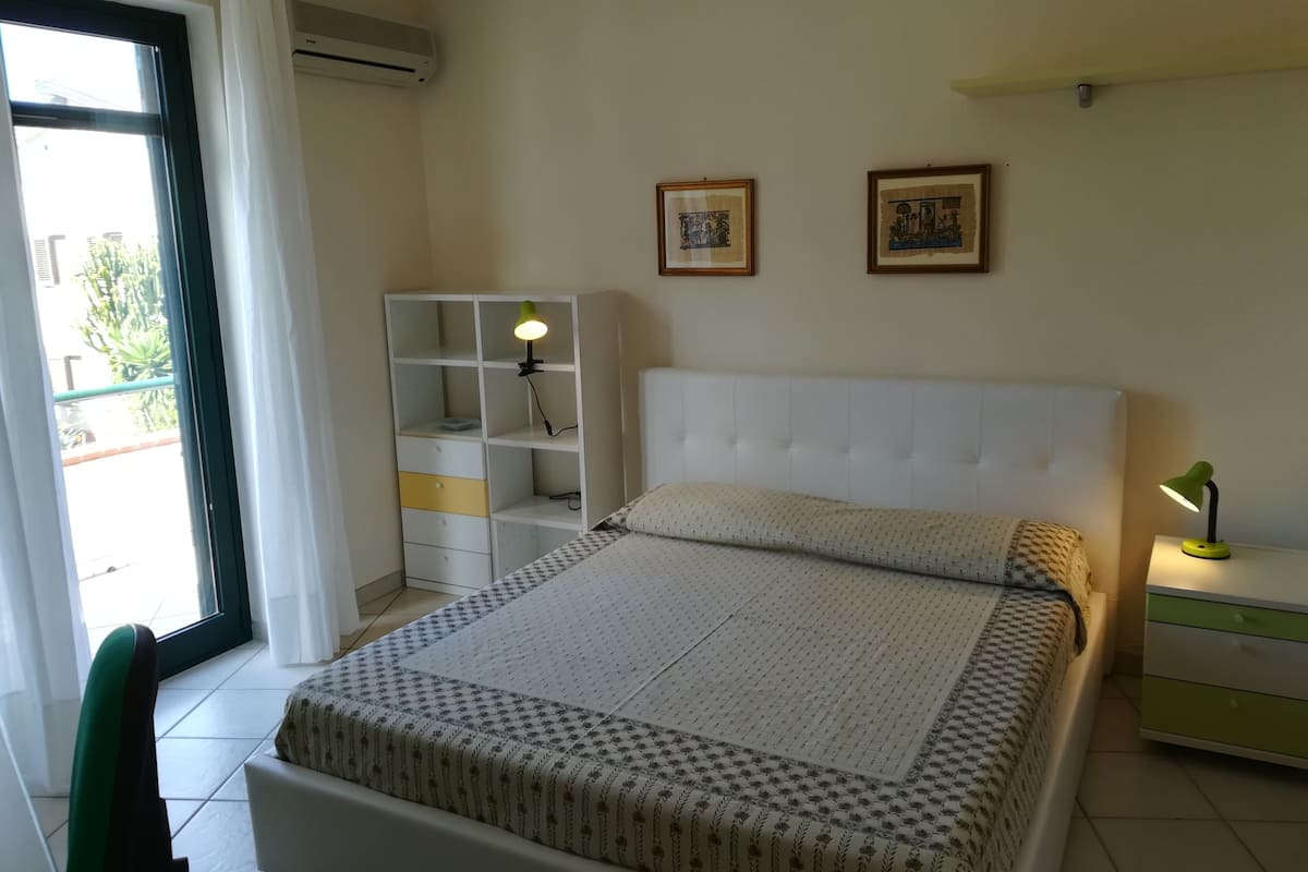 A bedroom with a bed, a nightstand, a wardrobe, and two framed pictures on the wall.