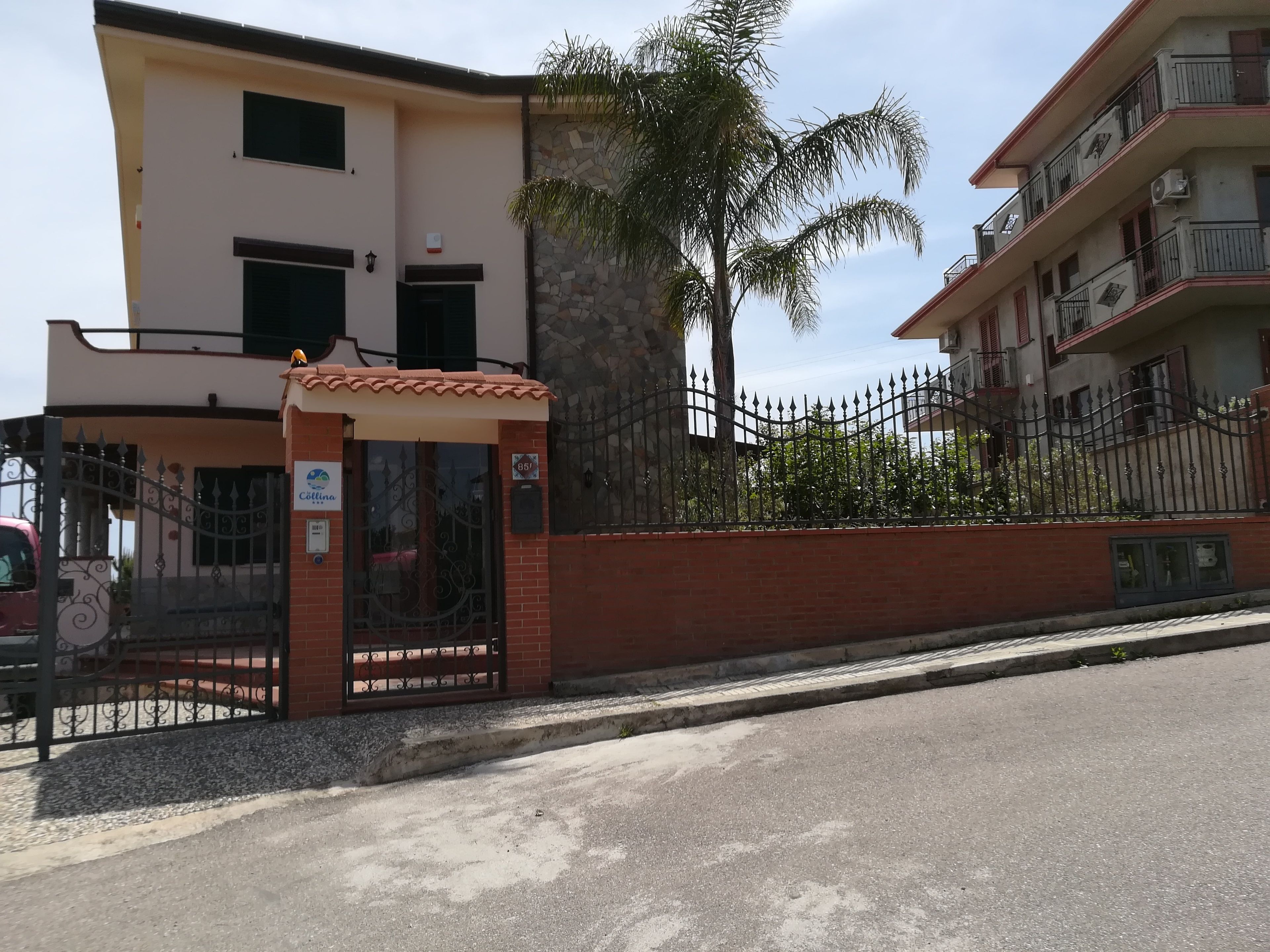 A multi-story building with a gated entrance, a small covered waiting area, and a stone wall.