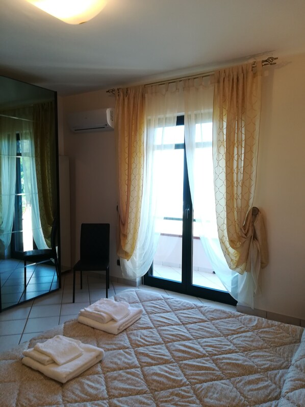 A bedroom with a bed, a chair, a large mirror, and a sliding glass door.