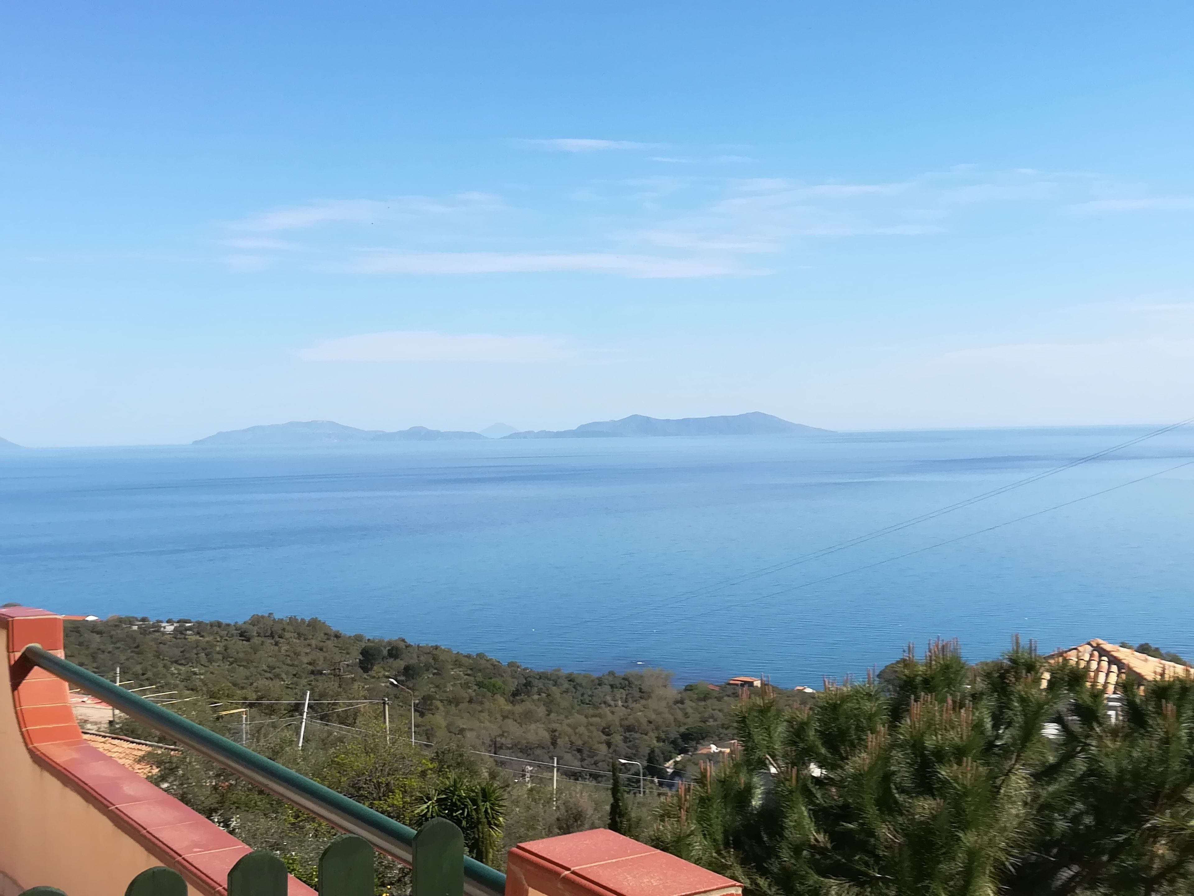 Vista costera con cielo despejado, montañas distantes y una extensión de agua.