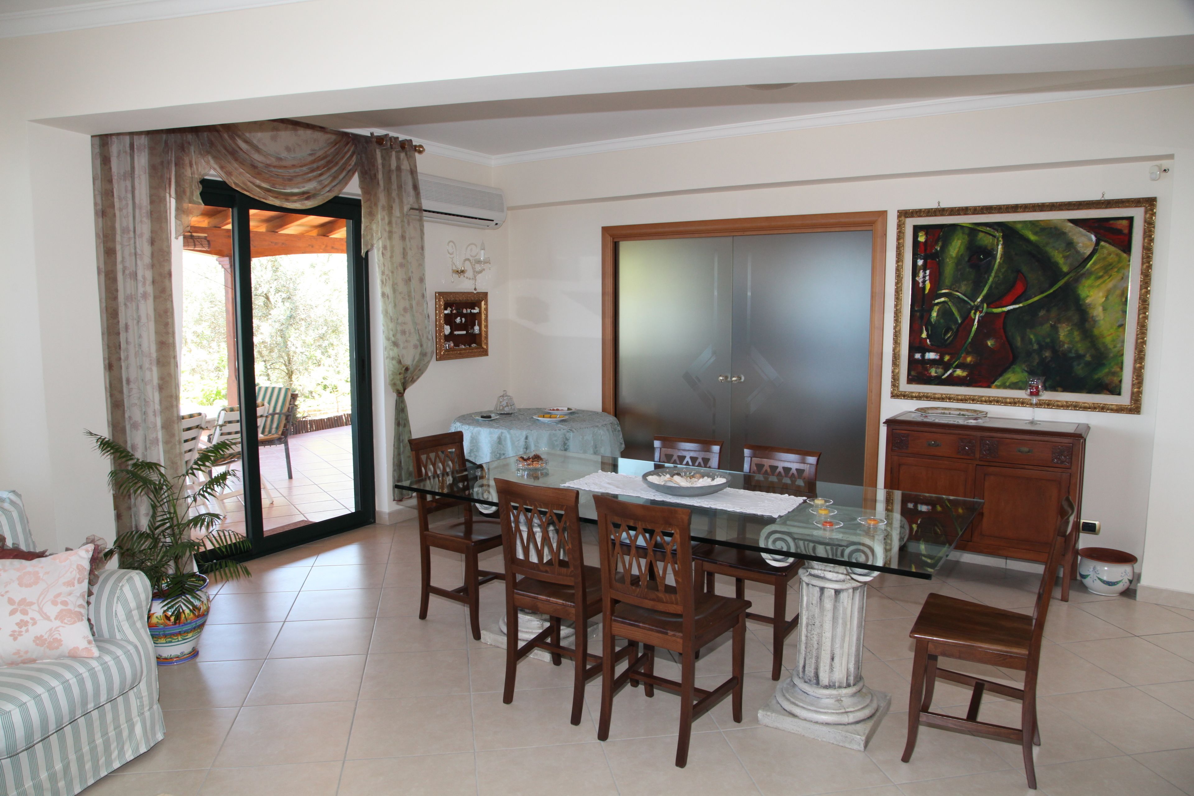 A dining area with a glass table, wooden chairs, and a view through a sliding glass door to an outdoor patio.