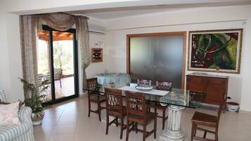 A dining area with a glass table, wooden chairs, and a view through a sliding glass door to an outdoor patio.