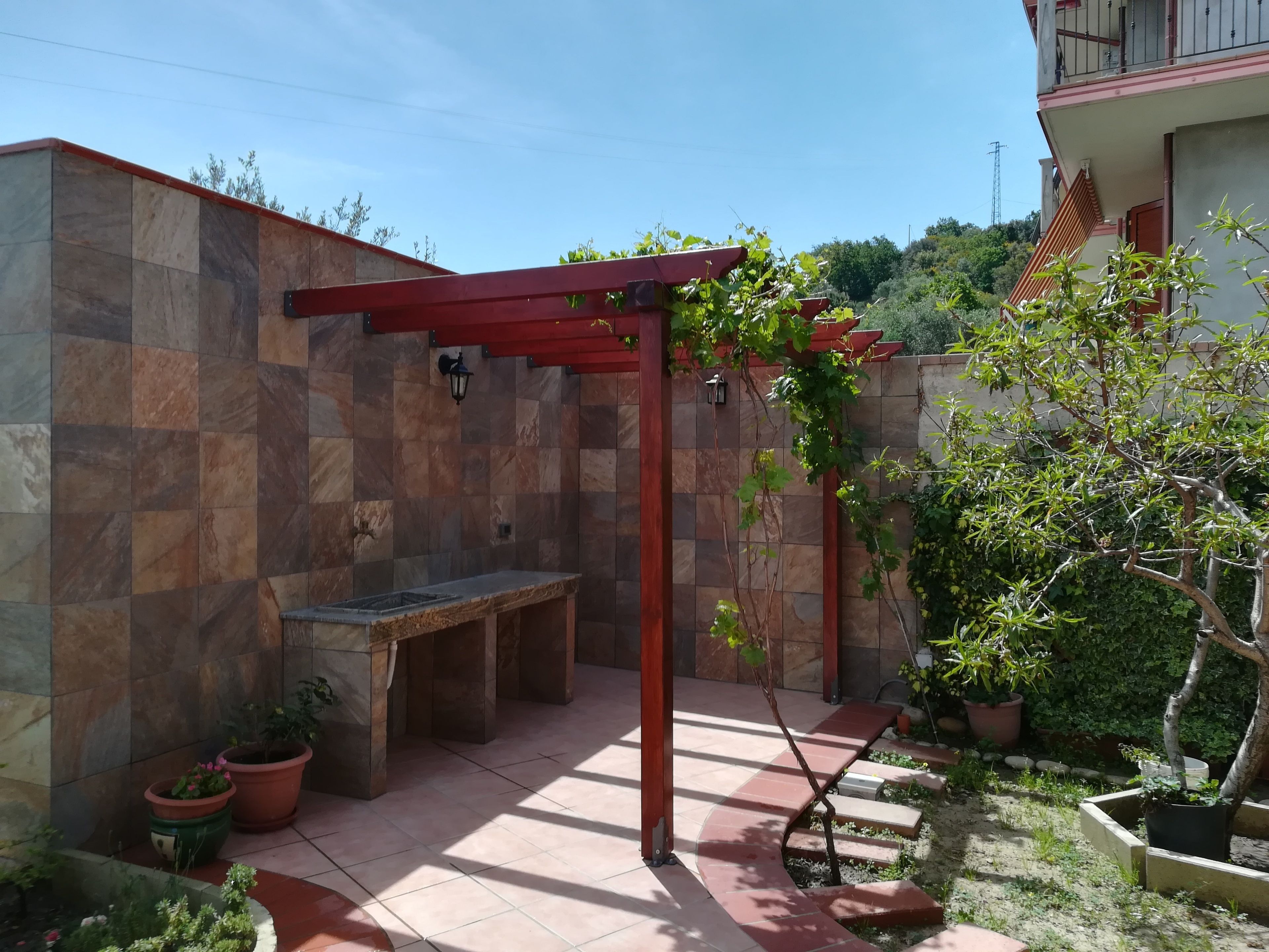 Un’area patio con un pergolato, una panchina e piante in vaso.
