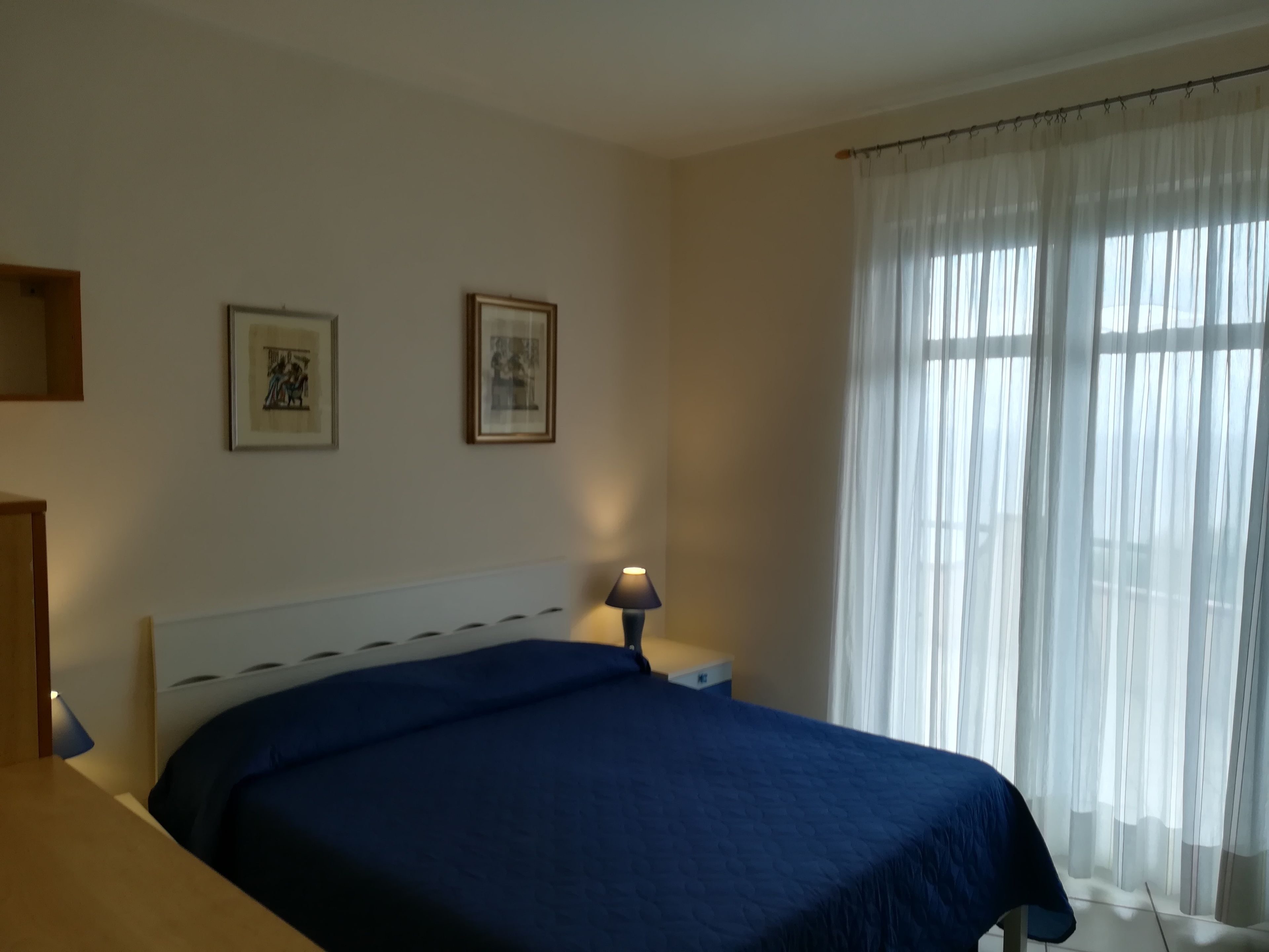 Un dormitorio con una cama, una mesita de noche, una lámpara y dos cuadros en la pared.