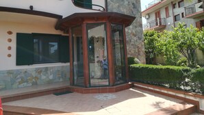 Esquina de un edificio con un quiosco de vidrio, un muro de piedra y un patio con baldosas.