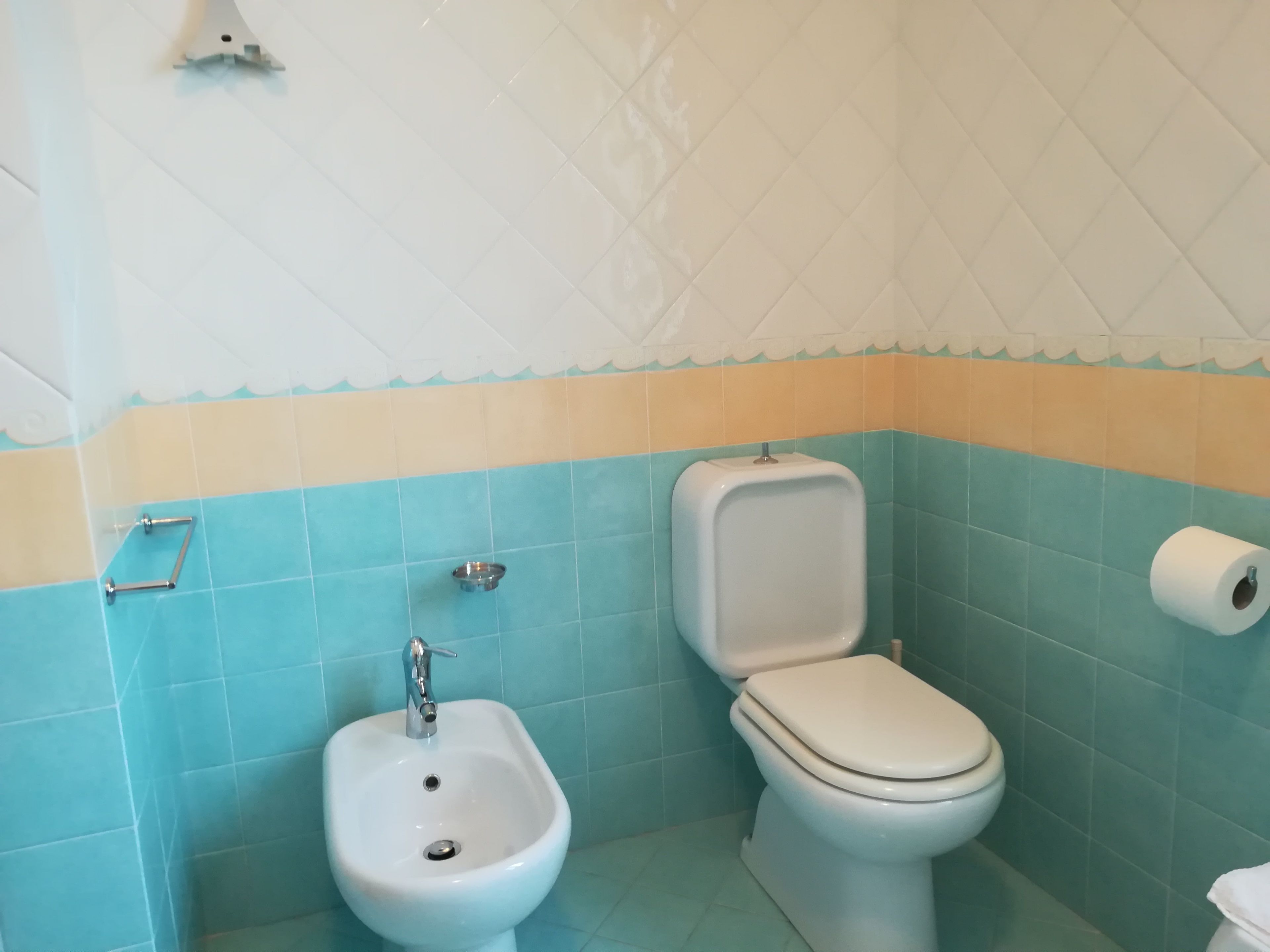 A bathroom with a bidet, toilet, and a roll of toilet paper on the wall.