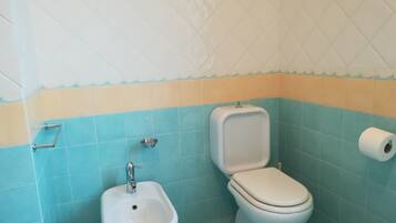 A bathroom with a bidet, toilet, and a roll of toilet paper on the wall.