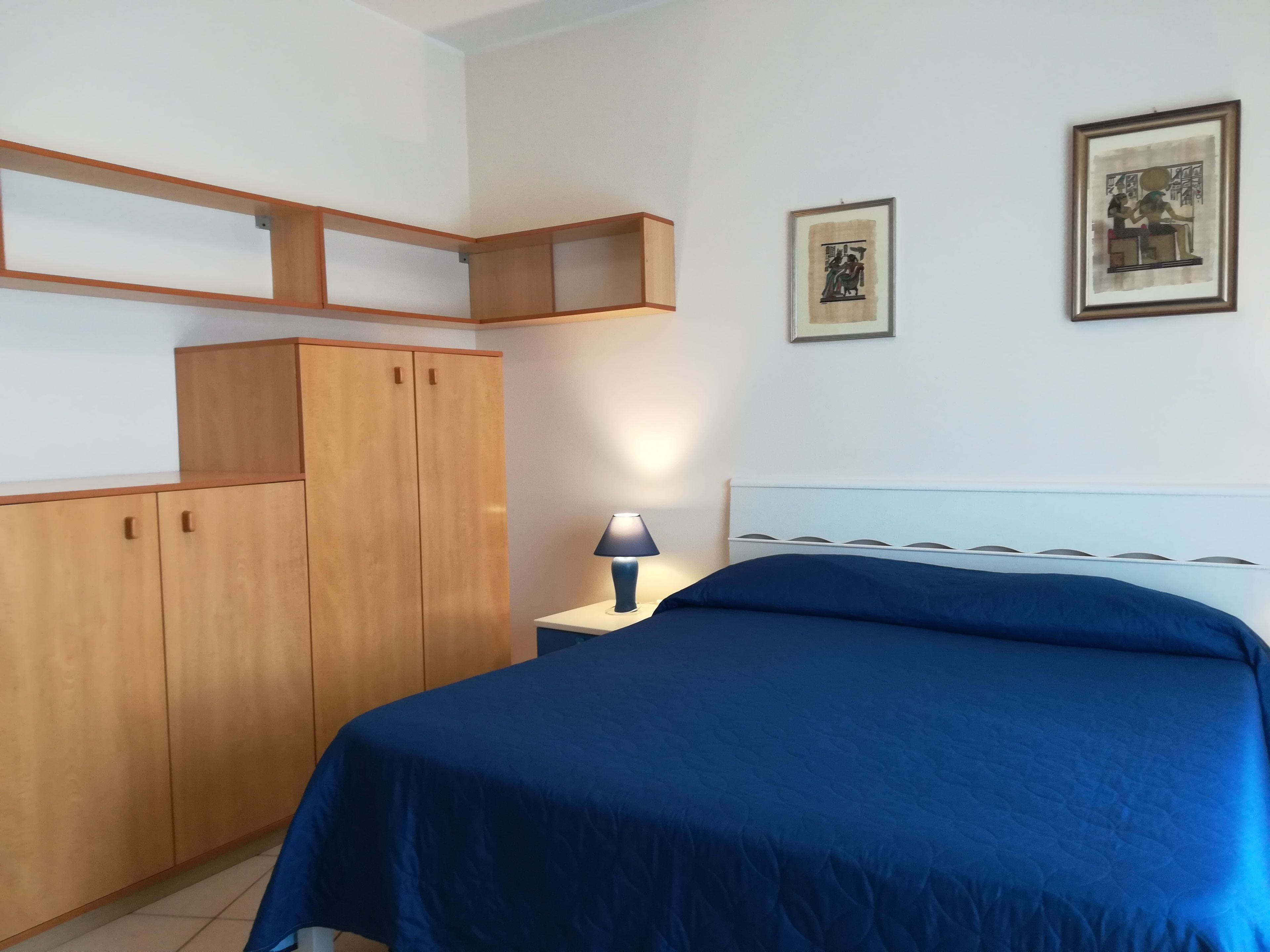 A bedroom with a bed, wooden wardrobe, and two framed pictures on the wall.