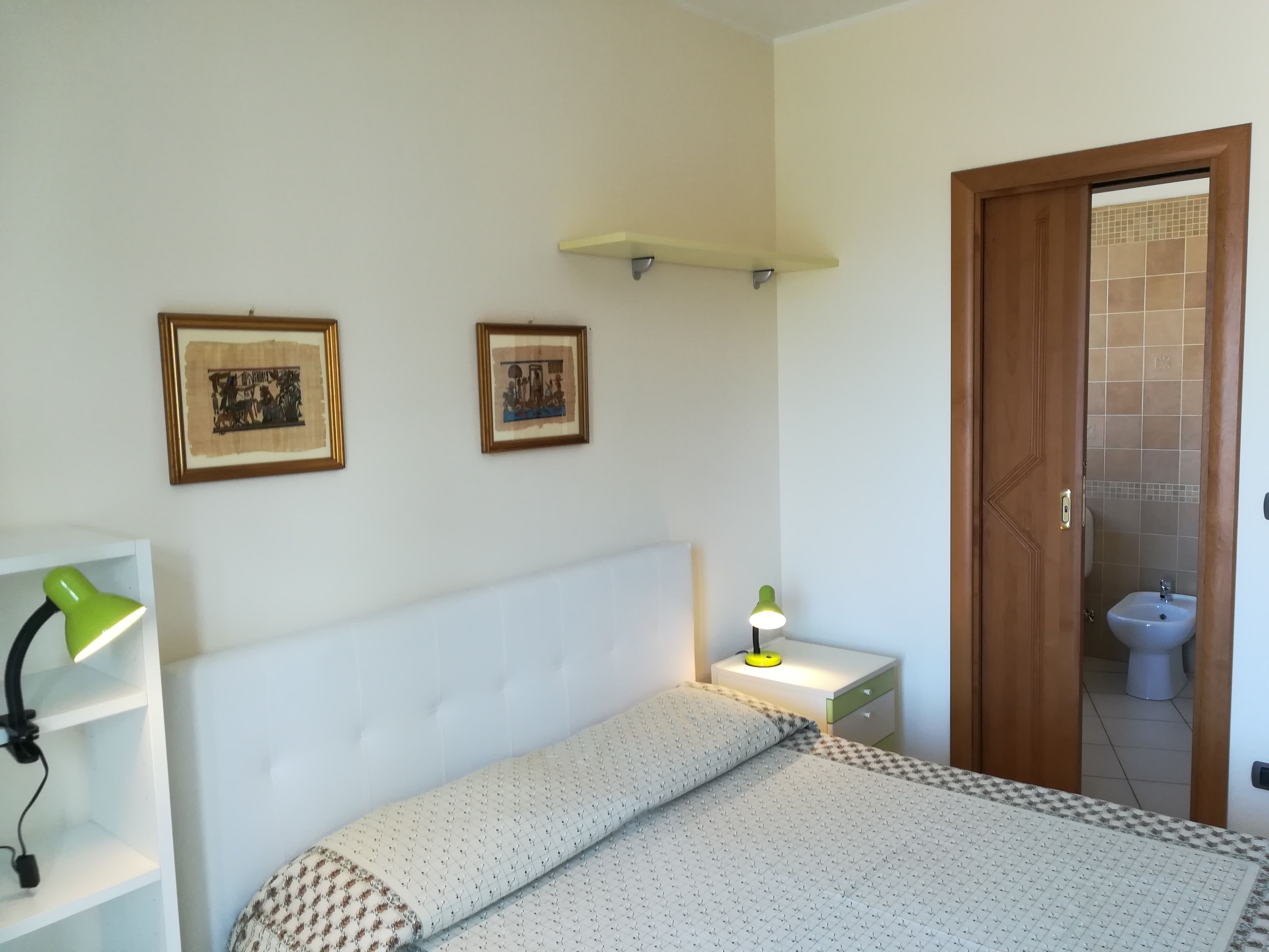 A bedroom with a bed, a bedside lamp, a nightstand, and a door leading to a bathroom.